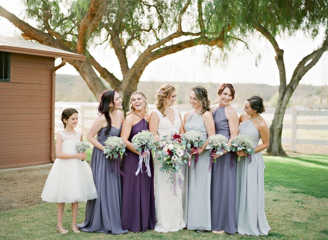 Bride posing with bridesmaids and flower girl with bridesmaids wearing varying hues of blue and purple