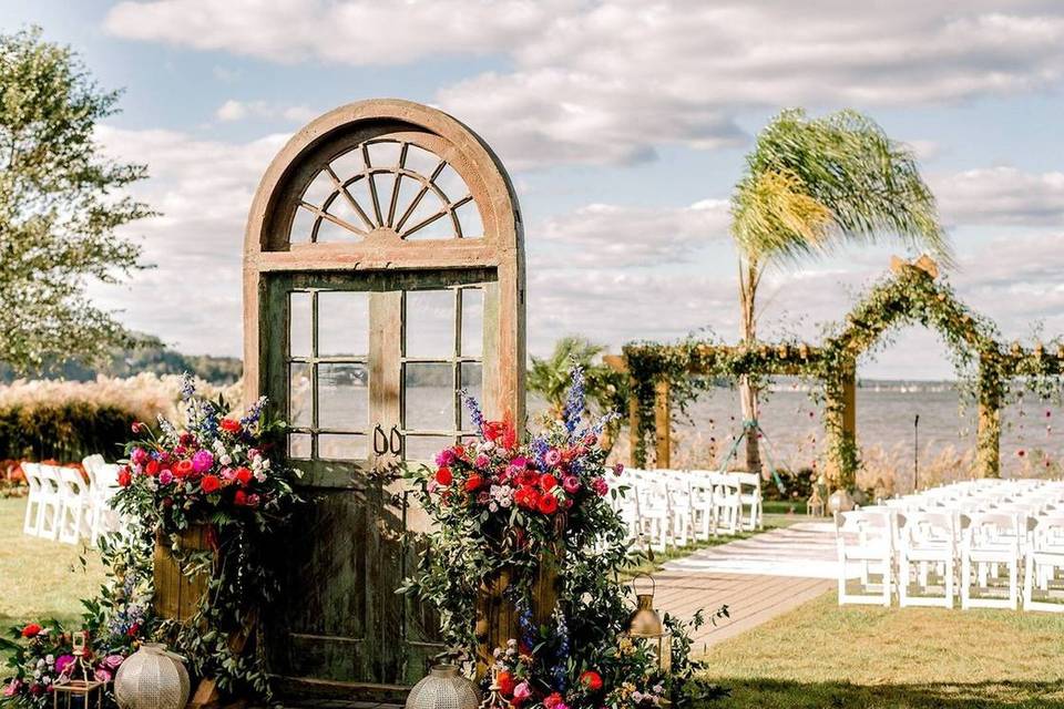 outdoor waterfront ceremony with reclaimed door at the start of the aisle decorated with flowers and vintage lanterns