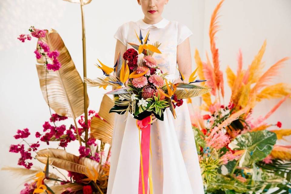 bride holding colorful summer wedding bouquet with birds of paradise, orchids, and tropical greenery