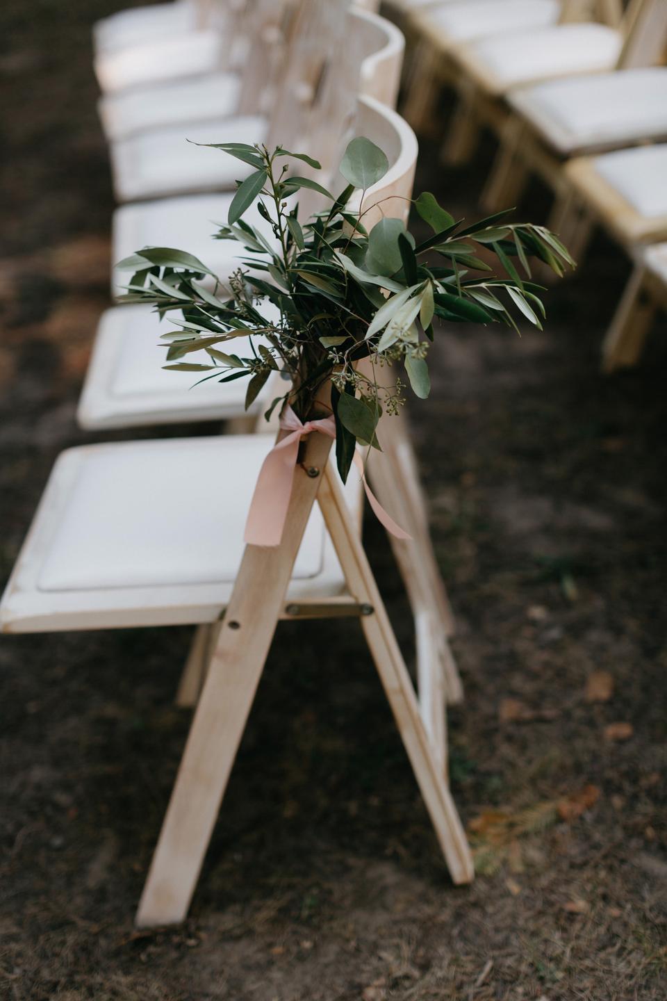 romantic outdoor wedding aisle decor greenery bunch tied to folding chair with blush pink ribbon