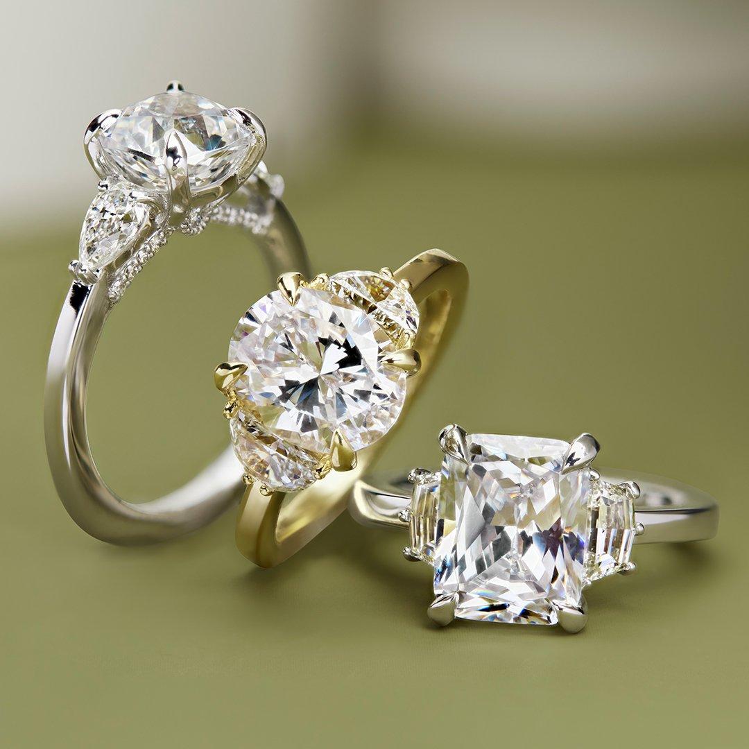 various three-stone engagement rings against green backdrop