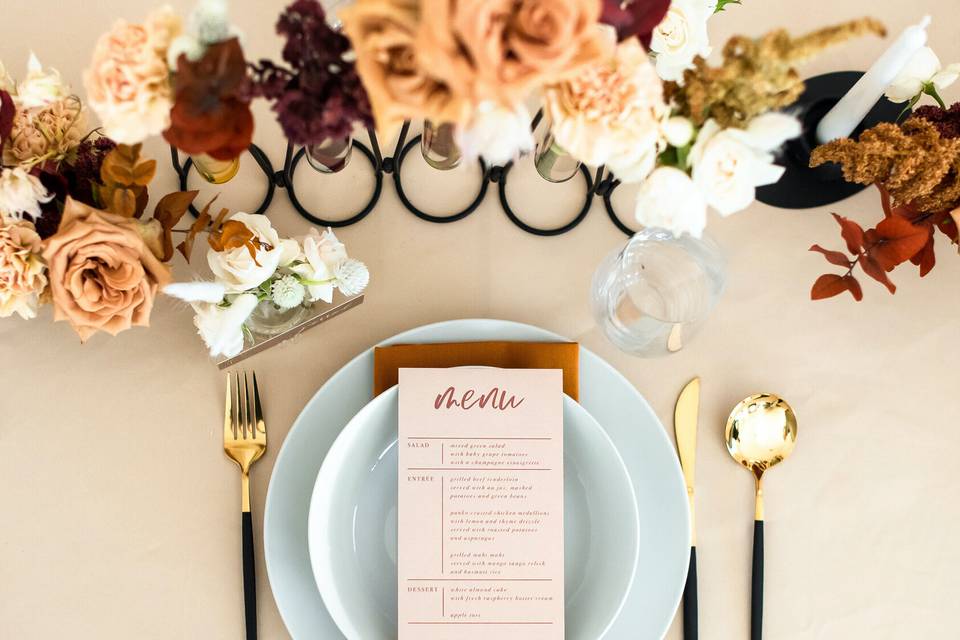 modern wedding tablescape with minimalist white tablecloth, light blue plates, black and gold silverware, and fall burgundy and rust orange centerpieces