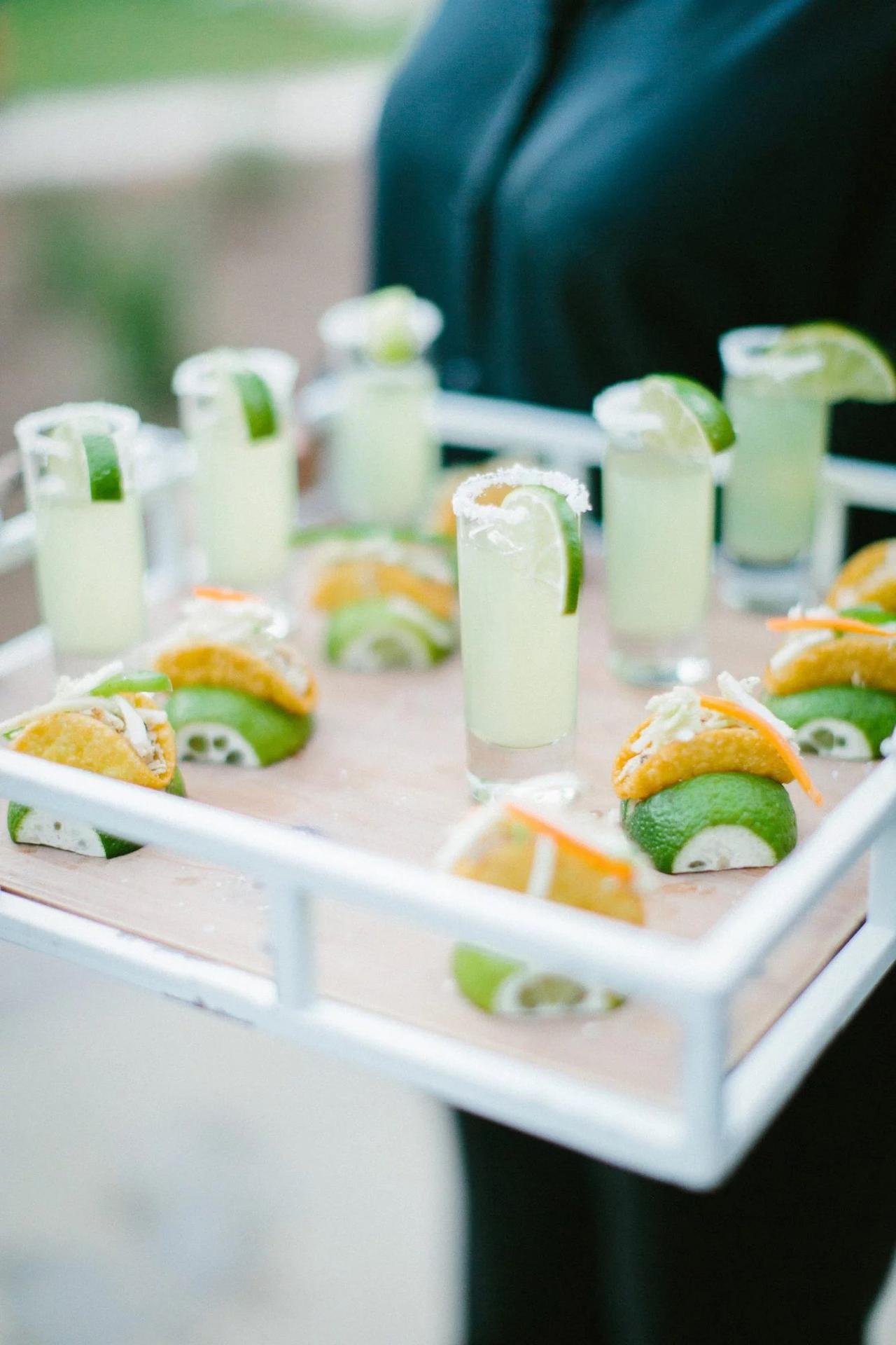 server holds a tray of mini shooters and bite size tacos in lime wedges