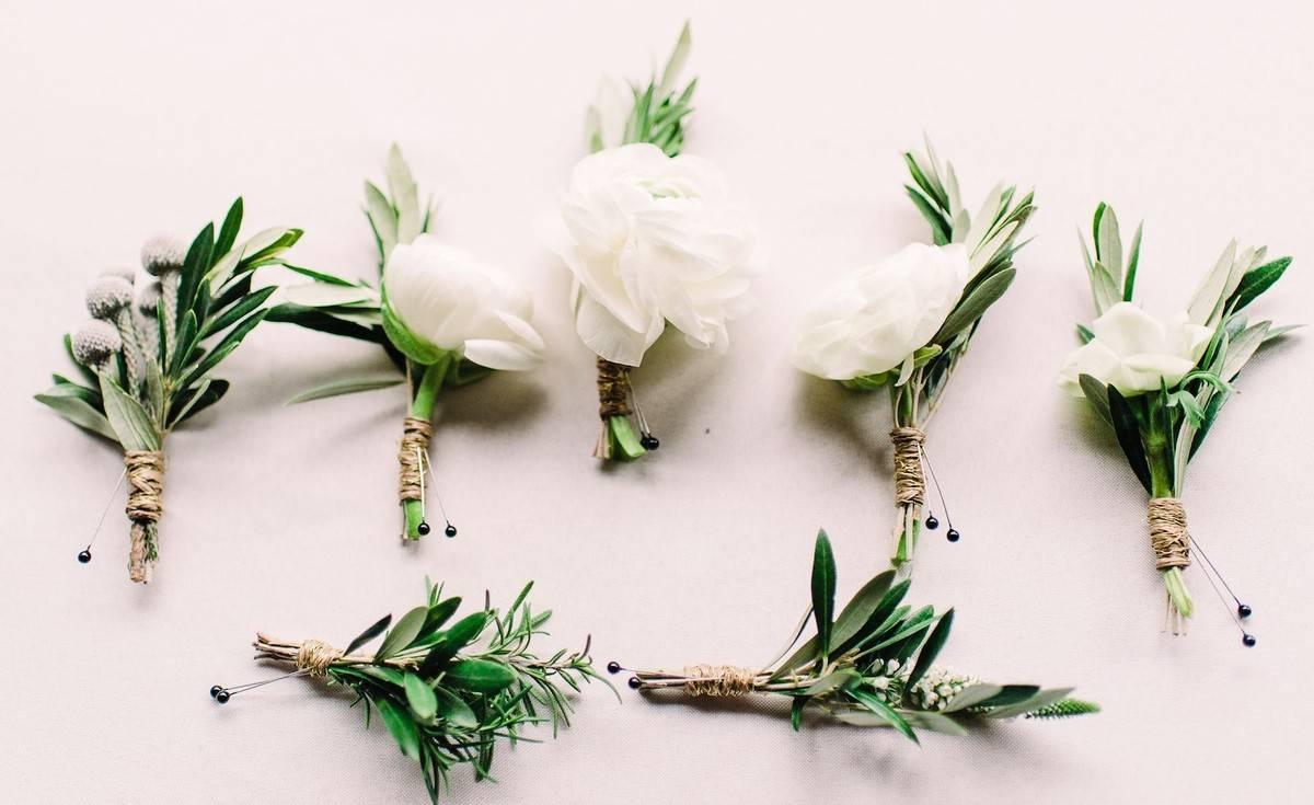 a row of greenery boutonnieres arranged side by side against white backdrop
