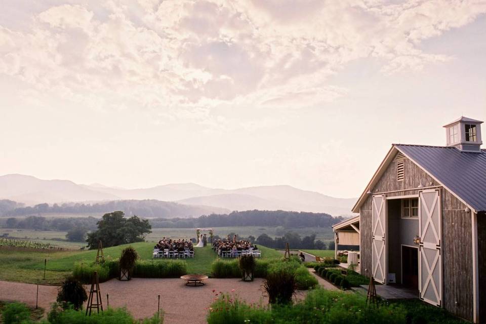aerial photograph of pippin hill farm in virginia barn on right side of frame with mountains and rolling hills in the distance at sunset