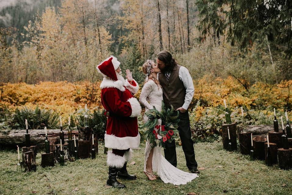 bride and groom kiss while wedding officiant in santa claus costume stands nearby