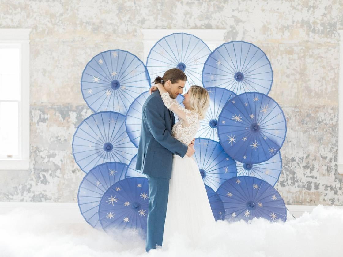 bride and groom stand in front of DIY wedding backdrop made from blue paper parasols painted with gold stars