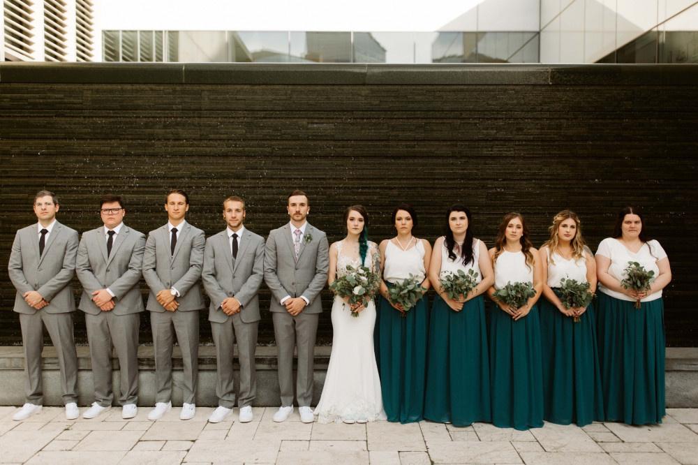 Wedding party photo with bride, groom, groomsmen, and bridesmaids with bridesmaids wearing teal skirts and white tops