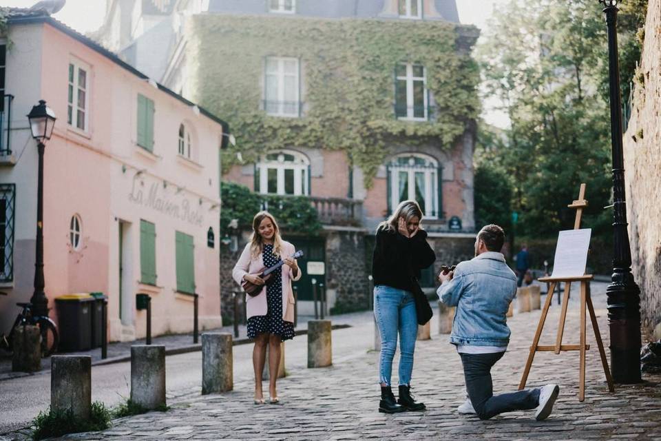 man proposing on one knee in paris cobblestone alley while guitarist stands nearby