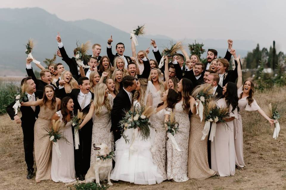 large wedding party cheering while bride and groom kiss