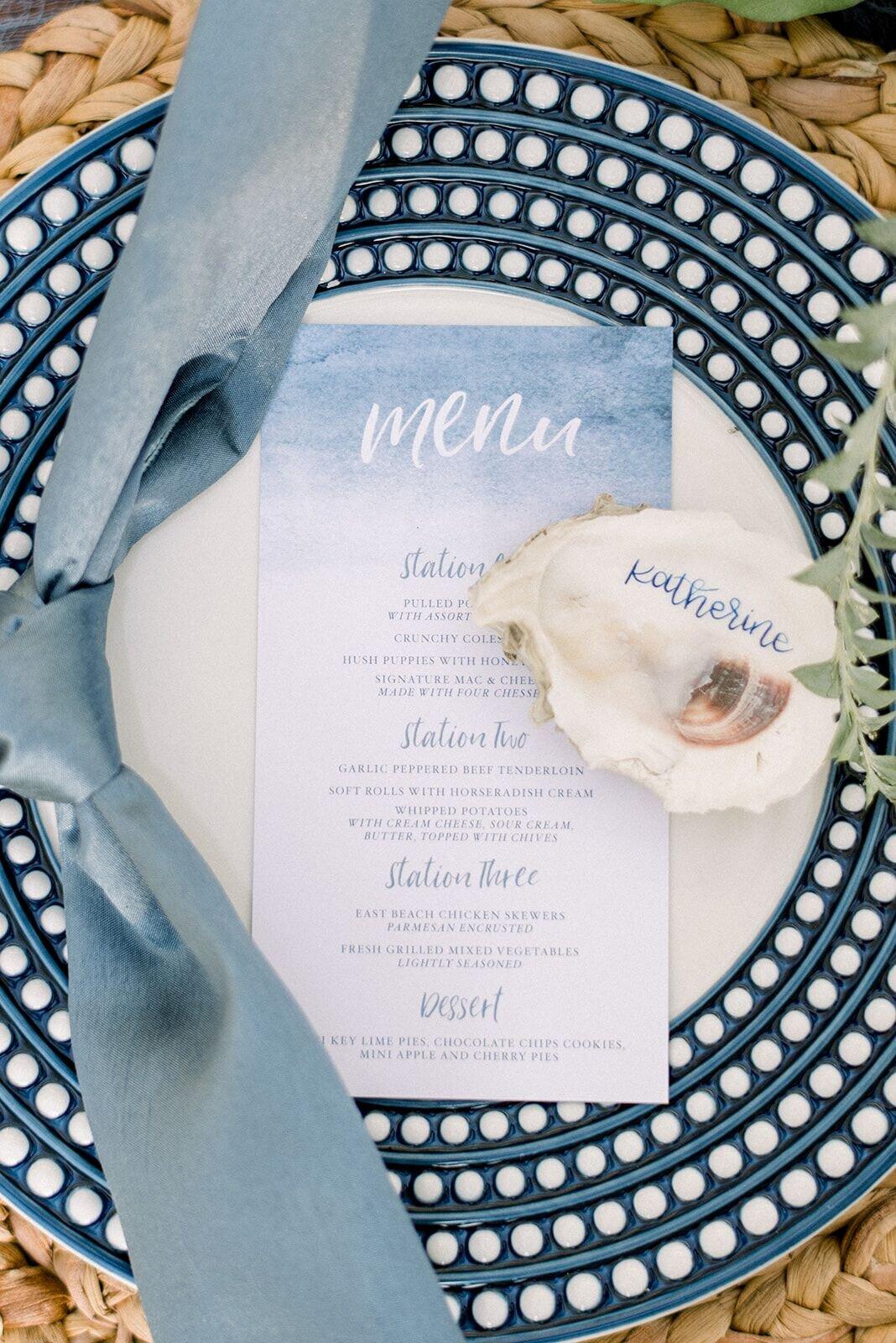 blue and white patterned dinner plate with blue watercolor menu card and oyster shell place card