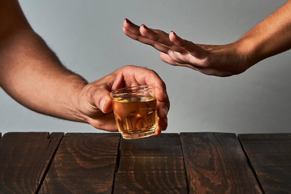 person holding shot glass while other person rejects it