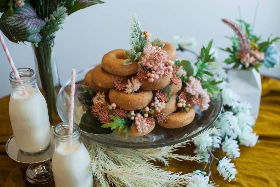 bridal shower dessert table with a tray of donuts decorated with flowers and milk in glass jars with pink striped paper straws