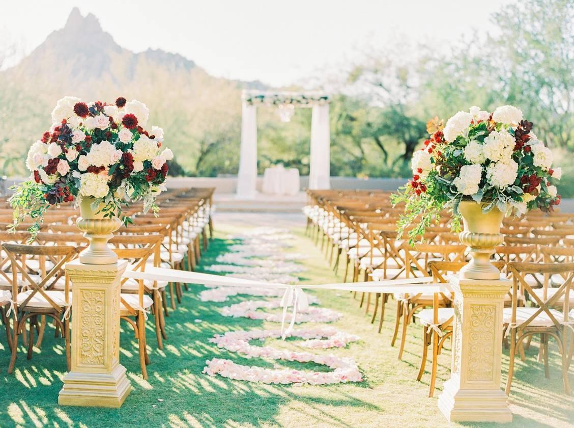 outdoor wedding ceremony with pink rose petals arranged in a swirling pattern down the grass aisle