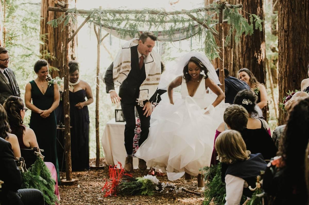 bride and groom jump over broomstick decorated with flowers