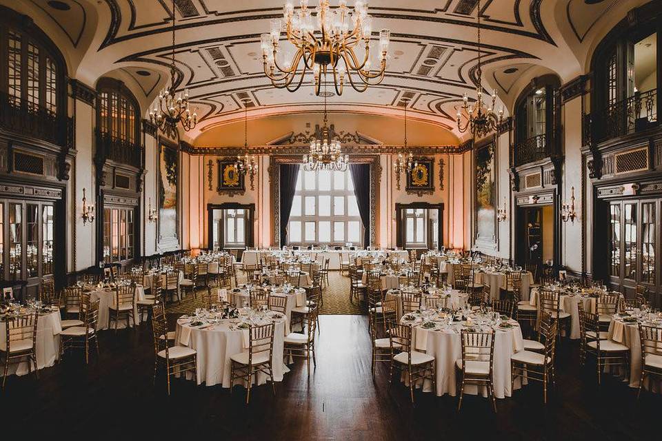 ornate ballroom with chandeliers set up for a wedding with gold chairs and ivory table linens