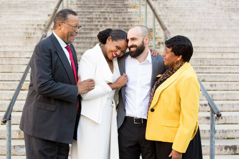 Newlywed couple hugs while standing with the bride's parents in front of NYC City Hall building