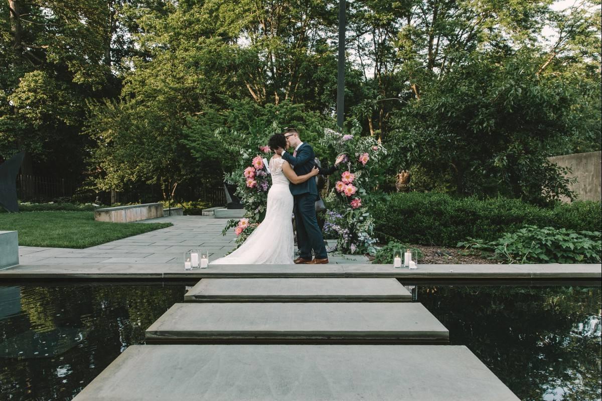 outdoor baltimore wedding venue bride and groom kissing while standing in front of reflecting pool in garden