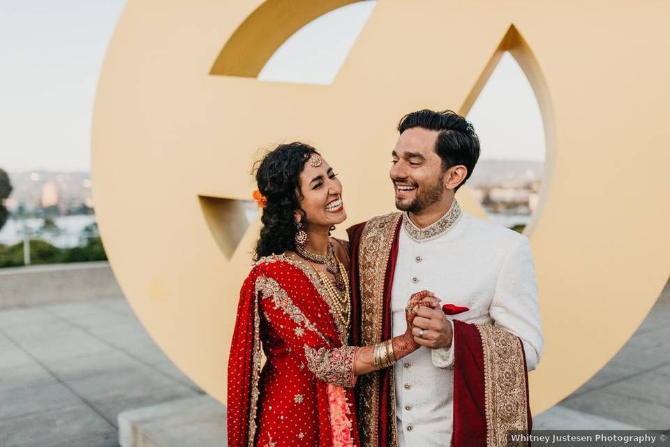 bride and groom laugh while standing in front of large peace symbol statue at oakland museum in california