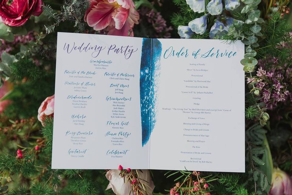 watercolor wedding ceremony program booklet is displayed on a bed of flowers and greenery