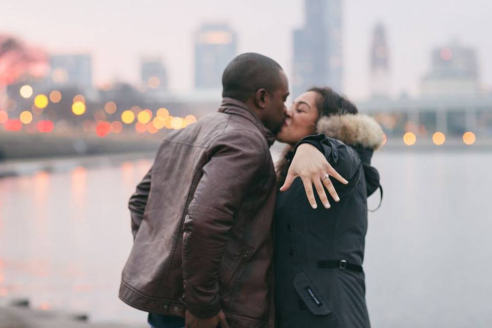 newly-engaged black couple kisses as bride shows her engagement ring off for the camera