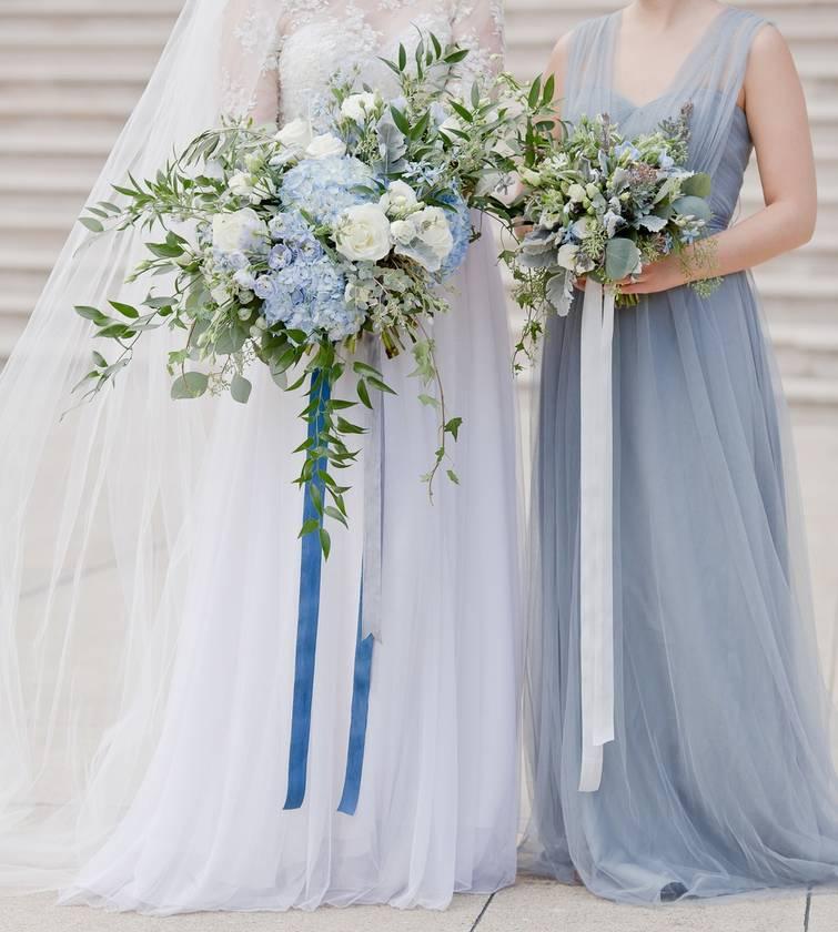 bride and bridesmaid holding bouquets with long blue and white ribbons