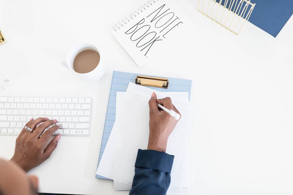 woman writing on paper on a clipboard surrounding by coffee mug and notebook