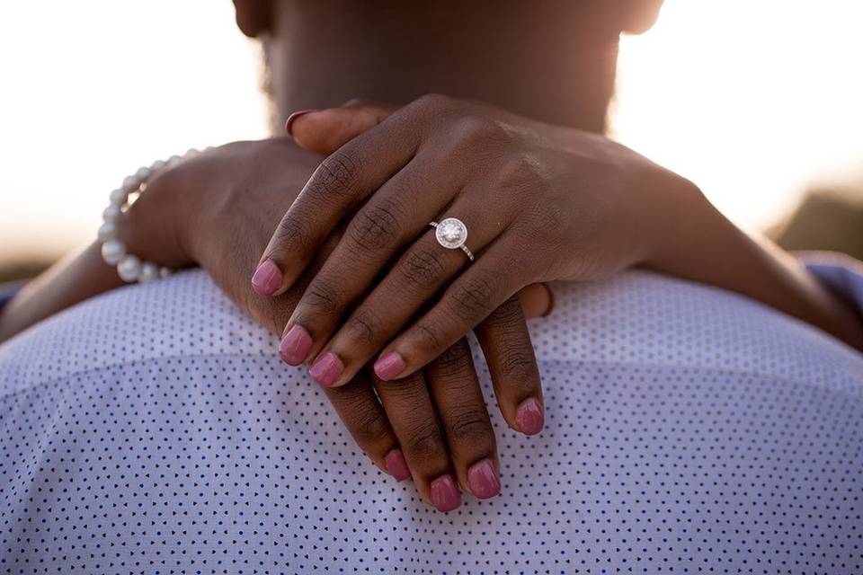 closeup of round halo engagement ring on bride's hand wrapped around groom's shoulders 