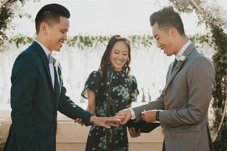 two grooms exchanging wedding rings with an officiant looking on