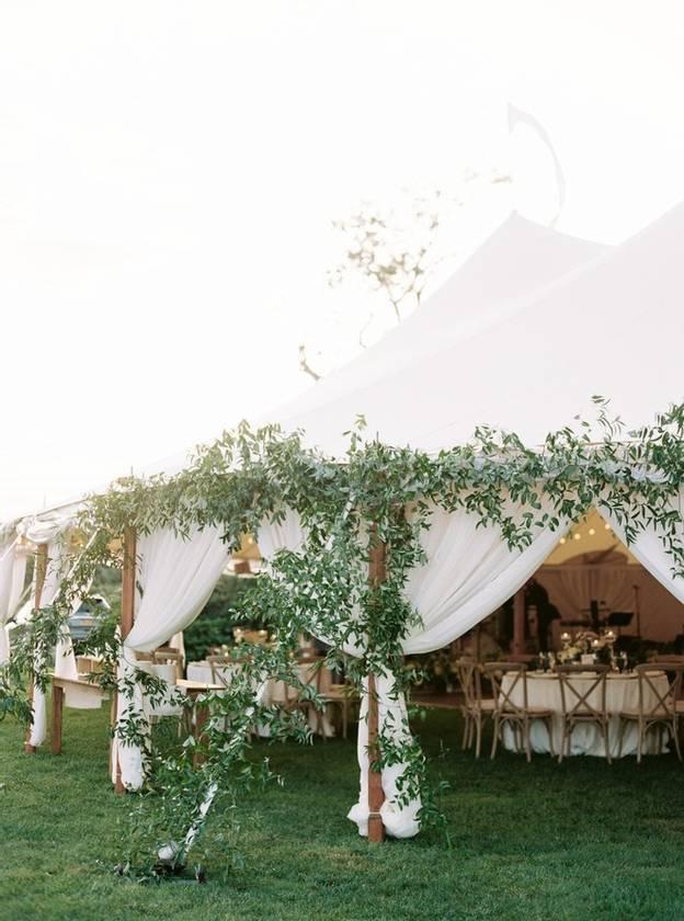 sailcloth wedding tent is decorated with greenery trailing up the posts and ropes