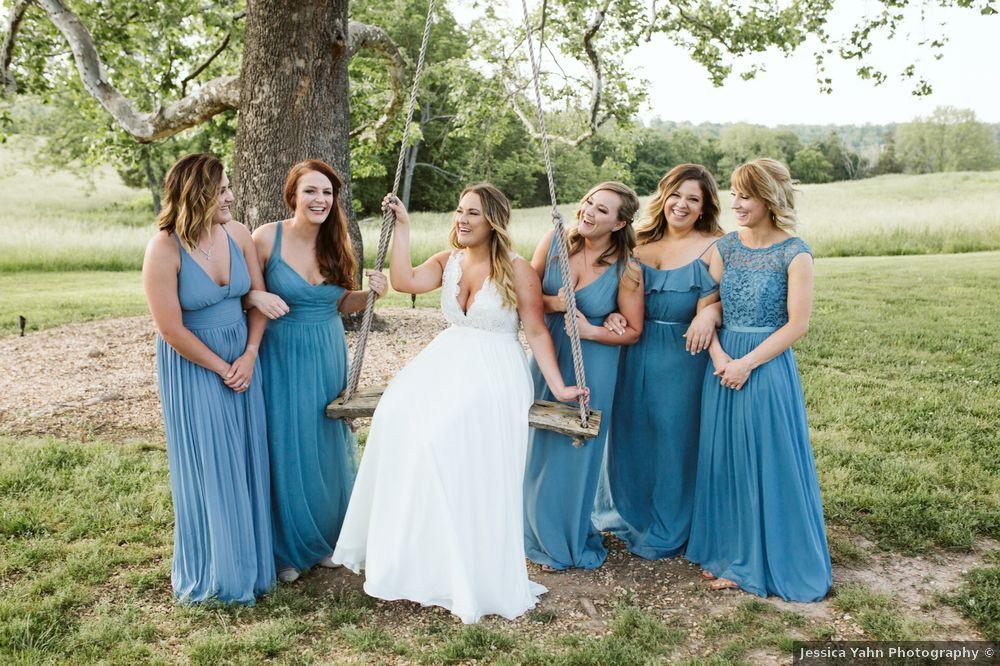 Bride sitting in tree swing with bridesmaids on either side smiling and wearing blue dresses