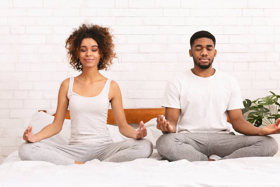 couple sitting side by side on bed and meditating