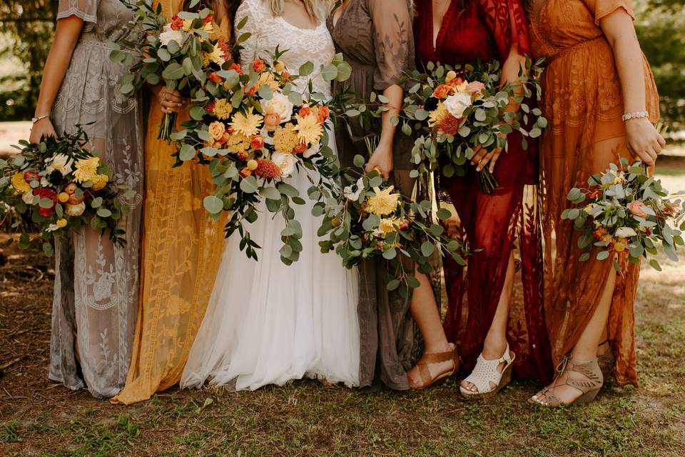 bridesmaids wearing fall colored dresses carrying bouquets of greenery and bright flowers