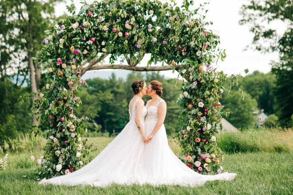 two brides kissing outdoor wedding ceremony with floral arch