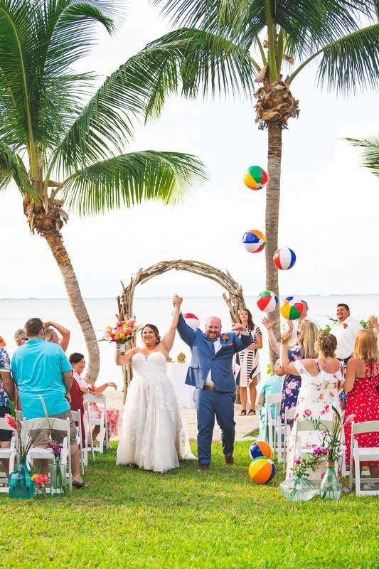 bride and groom walk down the aisle as guests toss beach balls in the air