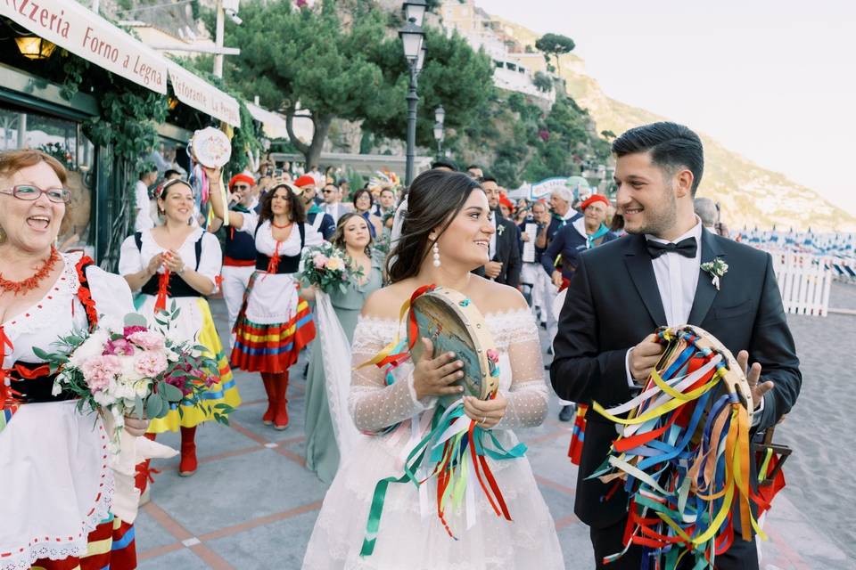 bride and groom hold tambourines while walking through amalfi coast town