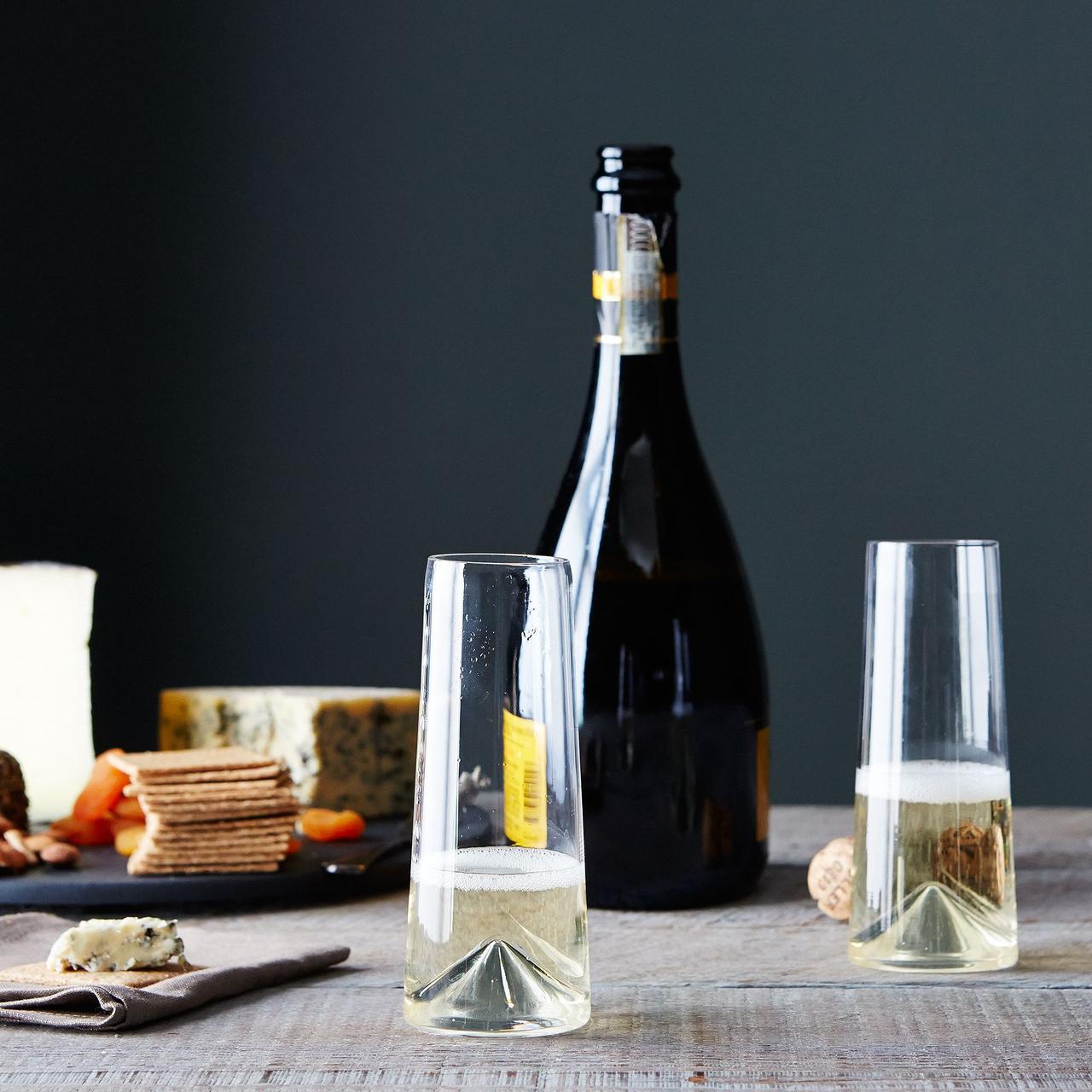Сервировка стола с сырной доской, бутылкой шампанского и двумя бокалами для шампанского без ножки