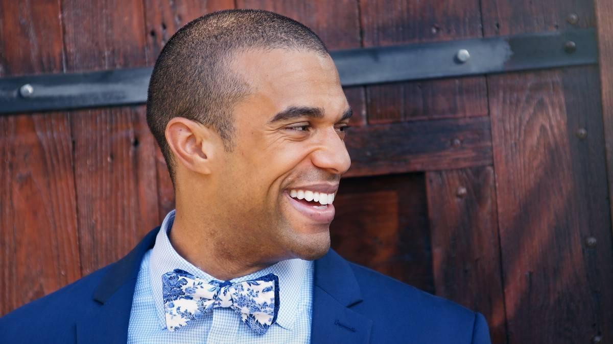 groom wearing a navy blue suit and blue gingham button-down shirt accessorized with blue and white floral print bow tie