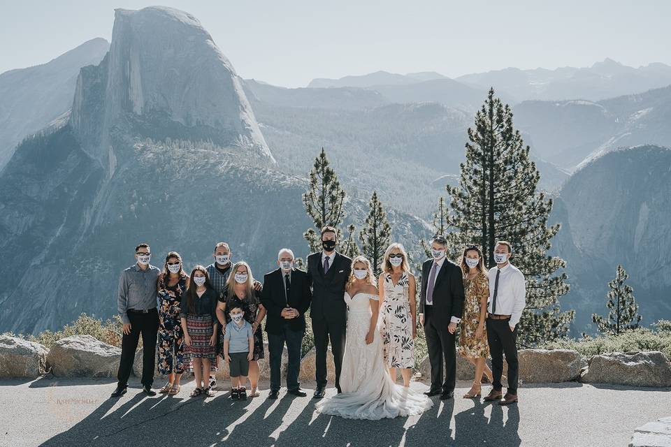 bride and groom stand outside in the mountains with small wedding party while wearing face masks