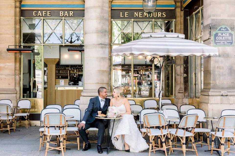 bride and groom in wedding attire sitting out front of french bistro in paris