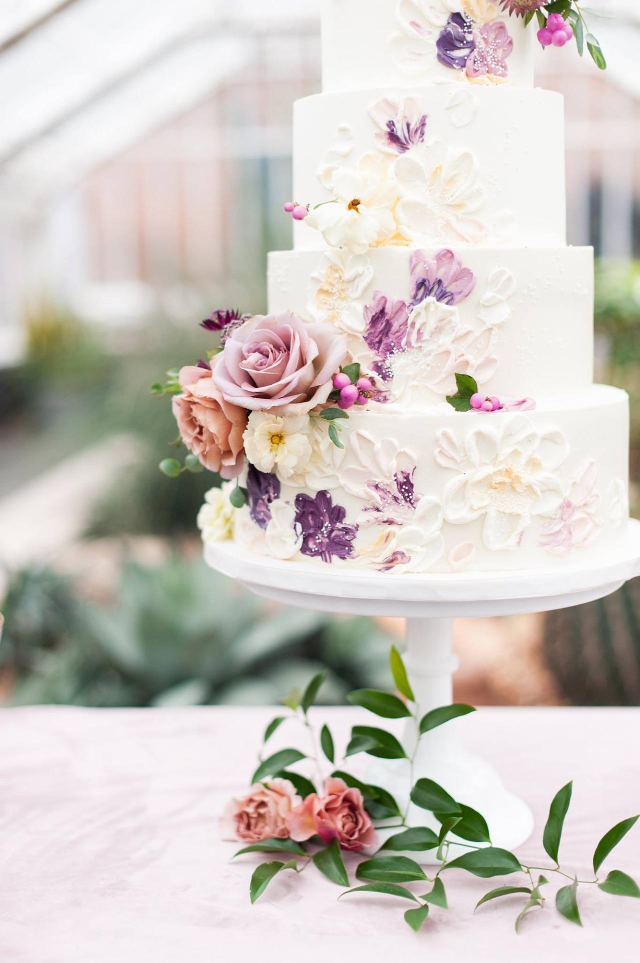 white four-tier wedding cake decorated with hand-painted buttercream flowers and fresh roses