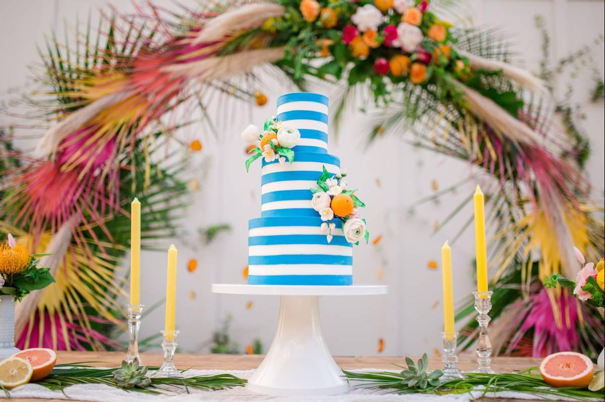 three-tier cake decorated with white and teal fondant stripes, orange ranunculus flowers