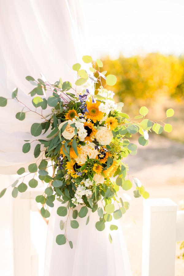 white sheer curtain tied back with sunflower arrangement of eucalyptus and white flowers