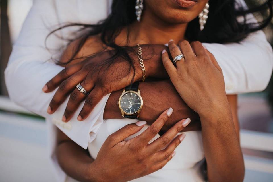 close up of Black couple's hands and arms as groom hugs bride from behind