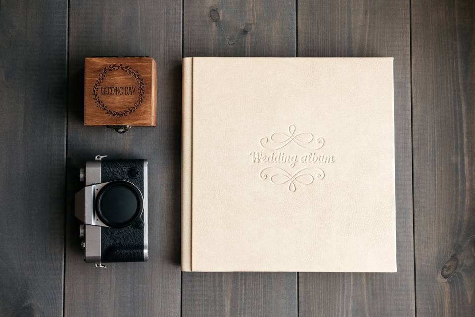 Off-white wedding photo album next to retro black camera and small wooden wedding keepsake box