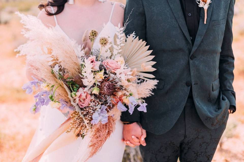 bride and groom holding hands with bride carrying boho bouquet