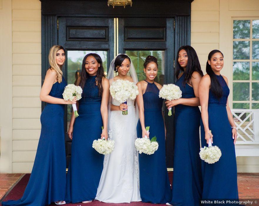 bride stands with her bridesmaids wearing navy blue matching floor-length gowns