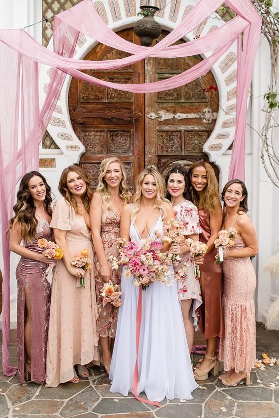 Bride smiling with her bridesmaids around her wearing mix and match pink dresses