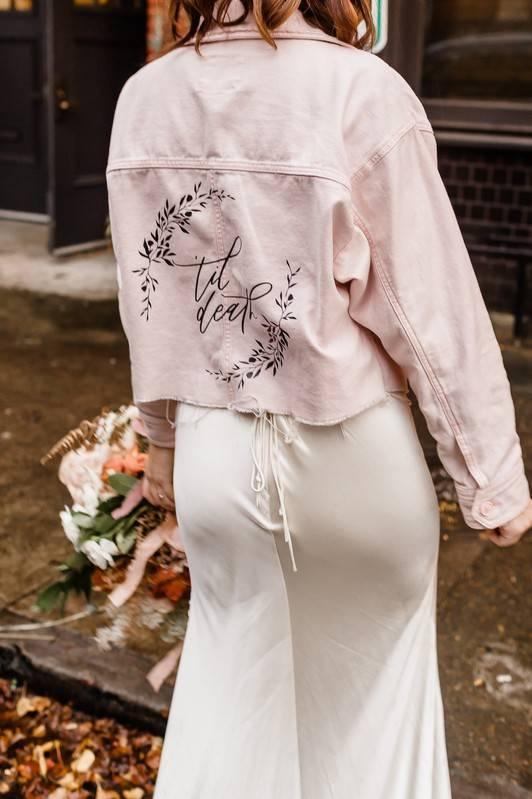 modern bride wearing pink leather moto jacket with "til death" written in black calligraphy on the back