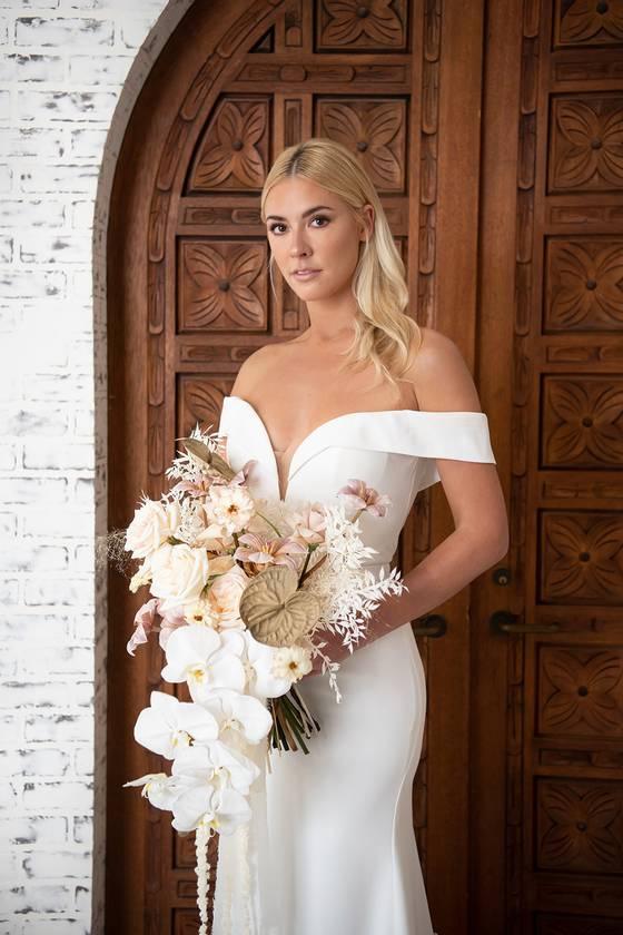 bride holding modern white and neutral summer wedding bouquet with orchids and bleached flowers